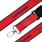 A red lanyard with black edges featuring the text Lufthansa in black, repeated along its length. The lanyard has a metal swivel hook and a black plastic buckle.