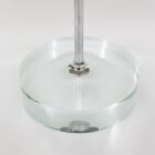 Close-up of a metallic rod attached to a round, transparent, and flat glass base on a white background. The glass base slightly reflects the light, emphasizing its smooth surface and clear material.