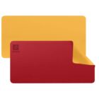 A red and yellow reversible desk mat is displayed. The yellow side is on top for the larger portion, while the red side shows partially, flipped to reveal the yellow underside. The mat features a logo and the text Lorem Ipsum on the corner.