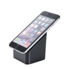 A smartphone with a silver edge is resting on a black, slanted docking station. The phones screen displays various app icons against a mountain wallpaper backdrop.
