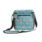A blue insulated cooler bag with a colorful tropical pattern featuring pineapples, starfish, and flowers. It has a black adjustable shoulder strap and side mesh pockets.