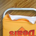 A close-up of a metal handle on an orange sign laying on a wooden floor. The sign has the word Deals partially visible, written in bold red letters. The top corner of the sign is slightly bent.