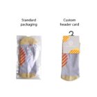 Two pairs of folded socks. The left pair is in clear plastic packaging labeled Standard packaging, and the right pair is attached to a gray card with orange stripes labeled Custom header card. Both pairs feature gray, yellow, and orange colors.