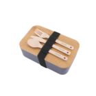 A bento box with a wooden lid, secured by a black strap. On top, there are wooden utensils—fork, spoon, and knife—labeled Victory. The base of the box is gray.