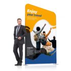 A man in a suit stands next to a travel-themed display featuring three people with backpacks joyfully raising their arms on a sunny day. The display has bold orange and blue colors with placeholder text.