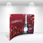 A red and gold promotional backdrop featuring a champagne bottle and festive decorations, including ribbons and baubles. The word CHAMPAGNE is prominently displayed in white text.