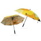 Two colorful umbrellas are shown. The first has a geometric pattern with orange and beige circles. The second features large yellow and orange shapes with a logo and text COMPANY NAME on one panel. Both have black handles.