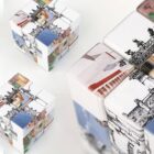 Close-up of three Rubiks cubes with illustrated images of architectural landmarks on each side. The cubes are arranged with different faces visible, showing parts of buildings and structures in various colors.