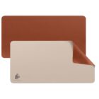 A reversible desk mat with one side brown and the other white, featuring a minimalistic logo in the corner. The mat is partially folded to show both colors.
