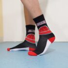 Person wearing black, white, and red socks with a basketball design and the word ESPORTS on each side. The socks contrast with the light blue floor and white wall in the background.