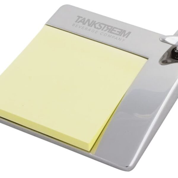 A silver desk accessory from Tankstream Beverage Company with a stack of yellow sticky notes and a built-in bottle opener on the top right corner.