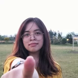 Person in glasses pointing at camera, ready to meet outdoors in a grassy area.