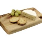 A wooden board with a wedge of brie cheese, a cluster of green grapes, and three round crackers arranged neatly.