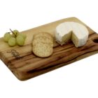 A wooden cheese board with a round of brie cheese partially cut, a few crackers, and a small bunch of green grapes.