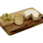 A wooden cutting board with a wheel of soft cheese partially sliced, three round crackers, and a small bunch of green grapes.