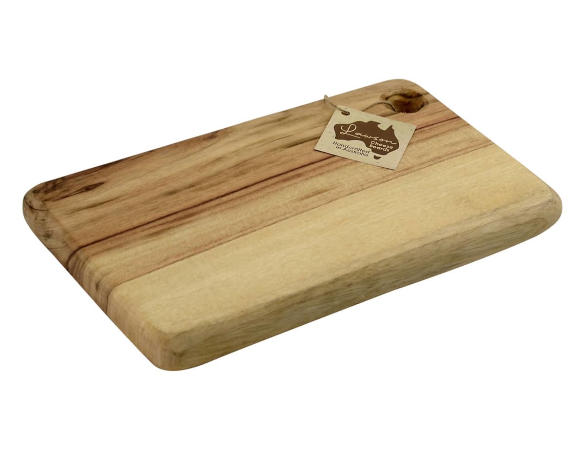 A rectangular wooden cutting board with a light brown and natural wood grain finish. It has a small tag attached to the corner with a string, featuring a logo and text.