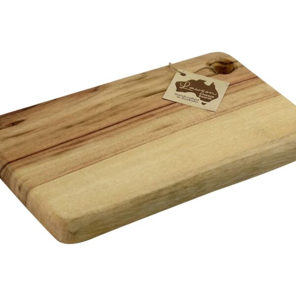 A rectangular wooden cutting board with a light and dark brown grain pattern. It has a small hole in one corner with a brown tag attached by a string. The tag features some writing and a logo.