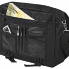 A black shoulder bag with multiple compartments and pockets. It contains items like pens, a notepad, and an electronic device, with an adjustable strap visible on the side. The bag is standing upright.