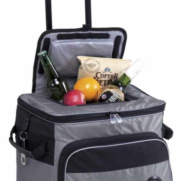 A gray rolling cooler with an open lid, revealing bottles, a bag of potato chips, an orange, and a red apple inside. The cooler has a telescopic handle, zippered compartments, and is equipped with built-in speakers. A connected smartphone lies beside it.
