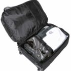 Open black suitcase with wheels, containing a pair of gray sneakers, a folded white shirt, and blue jeans. The suitcases interior is lined with black fabric.