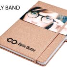 A notebook with a glittery cover features a belly band showing a close-up photo of a person wearing glasses. Text on the band reads Optic Outlet. An elastic band wraps around the notebook.