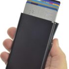 A hand holding a black cardholder containing several credit cards partially visible, with the cards slightly fanned out at the top.