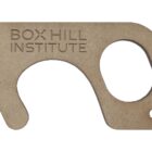 A beige, key-shaped tool with BOX HILL INSTITUTE engraved on it. It features a large circular hole and a hooked end, designed for hands-free interaction with surfaces.