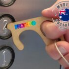 A hand uses a brown key-like tool branded Protego to press the number 2 button in an elevator. A Made in Australia label with an Australian flag is visible in the top right corner.