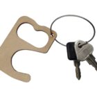 A tan, hook-shaped touch tool on a keyring with two metal keys attached. The touch tool has a finger hole and a hook for pulling or pressing surfaces without direct contact.