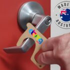 Hand using a tool to open a door handle. The tool is shaped like a hook and features colorful branding. A label reads Made in Australia next to an Australian flag. The door is red with a silver handle.