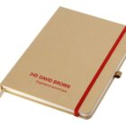 A closed, tan-colored notebook with a red elastic band and a ribbon bookmark. The cover features red text that reads DAVID BROWN and Engineered around you.