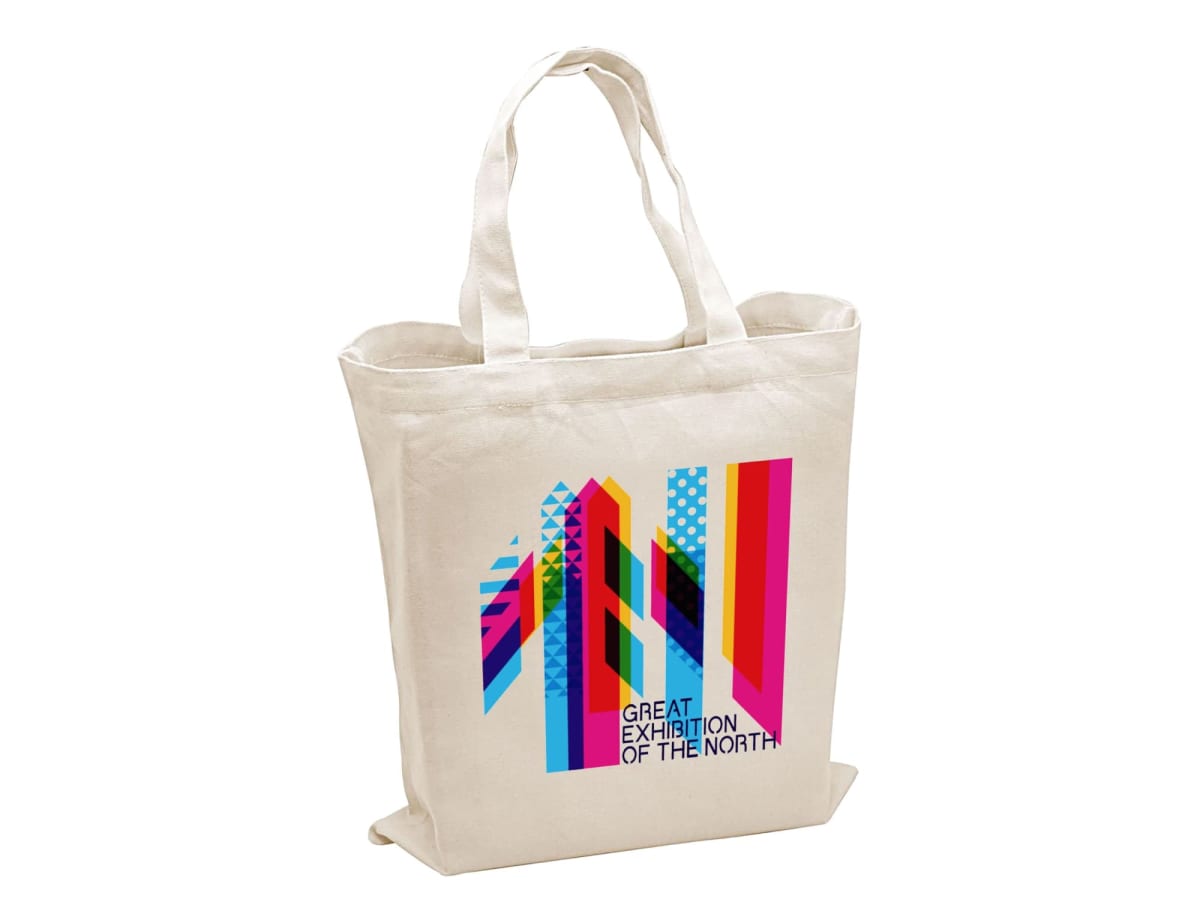 A white tote bag with colorful geometric patterns on one side, featuring text that reads Great Exhibition of the North.