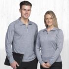 A man and woman wearing matching gray long-sleeve shirts with quarter zippers pose in front of a light-colored wooden background. The man holds a black folder, and both are smiling at the camera.