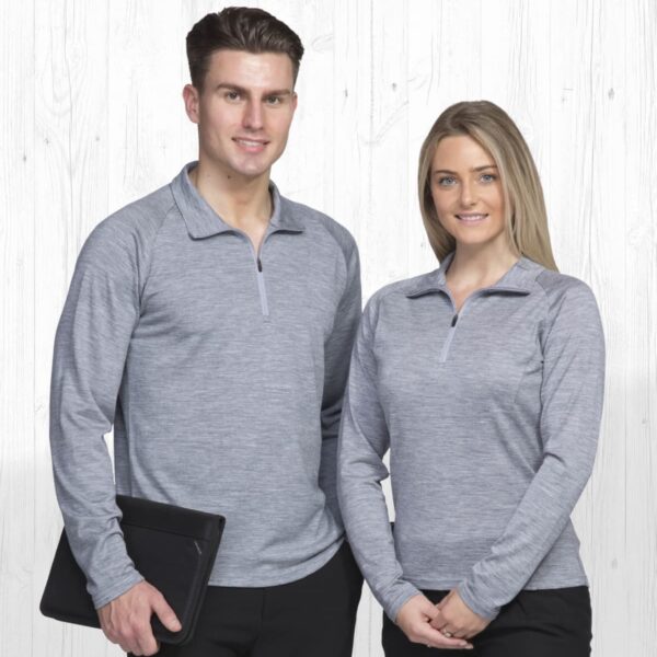 A man and woman wearing matching gray long-sleeve shirts with quarter zippers pose in front of a light-colored wooden background. The man holds a black folder, and both are smiling at the camera.