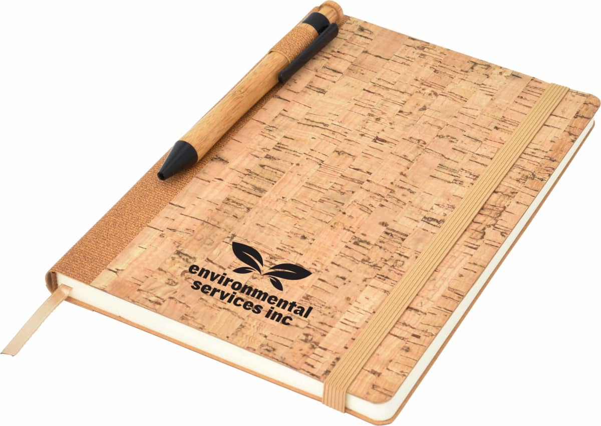 A cork-covered notebook with a pen attached to its spine. The cover features the logo and text environmental services inc along with a leaf design. An elastic band and ribbon bookmark are also visible.