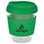 A clear glass travel mug with a green silicone lid and grip. The grip features the logo and text ABILITY PROJECTS in black.