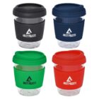Four reusable glass coffee cups with silicone lids and sleeves in black, blue, green, and red. Each cup features the Ability Projects logo printed on the sleeve.