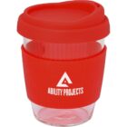 A reusable glass coffee cup with a red silicone lid and sleeve. The sleeve features a triangular logo and the text ABILITY PROJECTS in white.