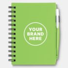 A green spiral notebook with a green pen attached on the right side. The cover features a white circle with the text YOUR BRAND HERE in the center.
