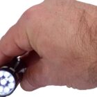A hand holding a lit flashlight with multiple LED bulbs, emitting a bright white light. The flashlight is cylindrical and black, and the hand holding it is positioned from the top view.