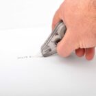 A person’s hand using a correction tape dispenser to cover text on a white paper.