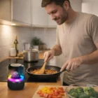 Smiling man cooks with Hands-Free Call Bluetooth Speakers on the kitchen counter.