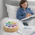 A girl writes in a notebook on a bed with books and Havant Bamboo Bluetooth Speakers nearby.