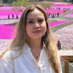 Team member in a white shirt stands before vibrant pink and purple blooms under a clear sky.