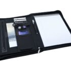 An open black zippered portfolio with a notepad, pen, USB cable, smartphone, a tablet, and pockets holding brochures and cards. The portfolio has compartments for organizing office or travel essentials.