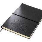 A closed black hardcover notebook with an embossed design on the cover. It has a black elastic band and a ribbon bookmark. The edges of the pages are visible and the cover appears smooth.