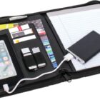 An open black zippered portfolio displaying a smartphone, a pen, two USB drives, cards, a power bank with a connected cable, and a lined notepad on the right.