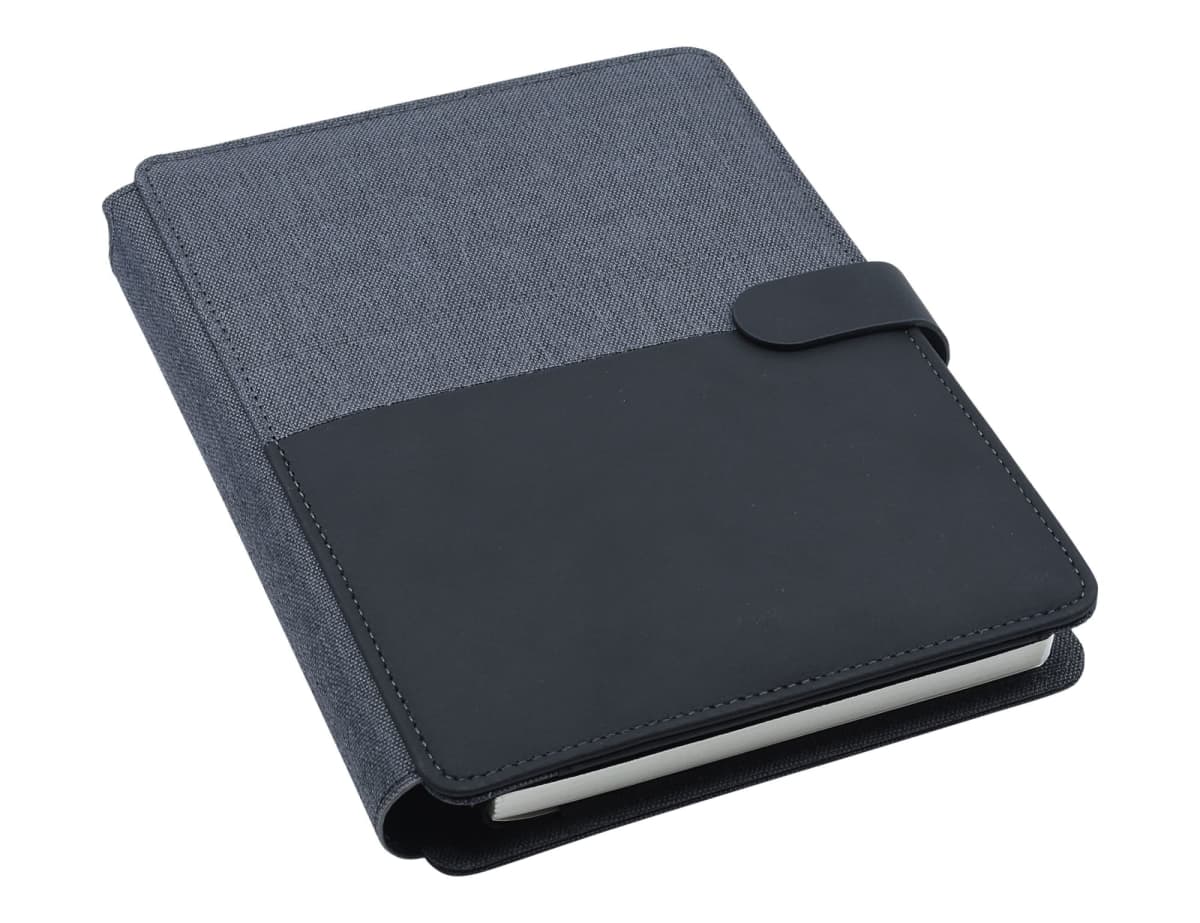 A closed notebook with a gray fabric cover and black leather accent, featuring a strap with a snap closure, resting on a white surface. The edges of the pages are visible, showing a clean and modern design.