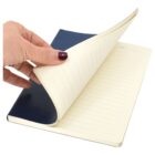 A hand with dark nail polish flips through a lined notebook with a blue cover. The pages are slightly curved, and theres a section for the date at the top of each page.