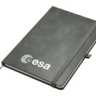A dark gray hardcover notebook with the ESA logo on the front. It has an elastic band closure, a pen holder, and a ribbon bookmark.